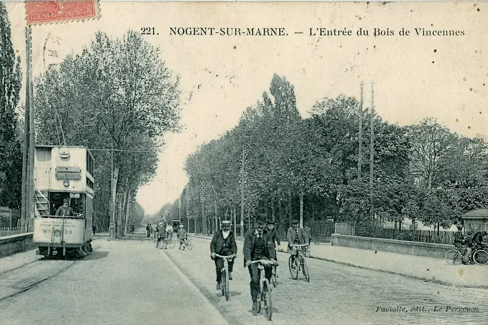 Carte postale ancienne : cyclistes et tramway sur une large avenue bordée d'arbres à l'entrée de Nogent-sur-Marne