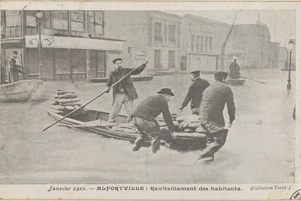 Carte postale de janvier 1910 : des hommes en barque ravitaillent les habitants dans une rue inondée d'Alfortville
