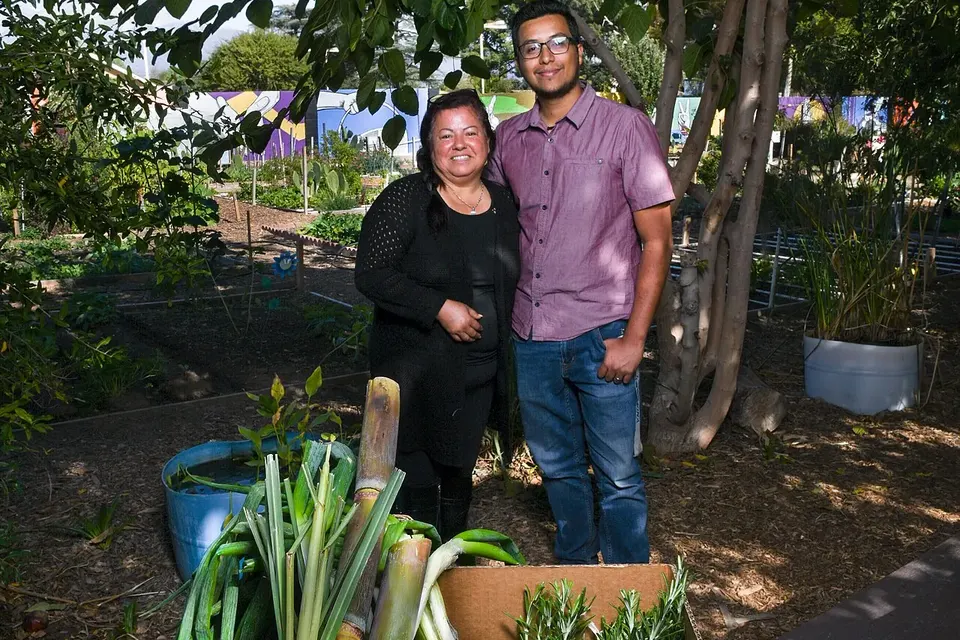 Deux personnes souriantes dans un jardin maraîcher, devant une caisse de poireaux et de légumes fraîchement récoltés