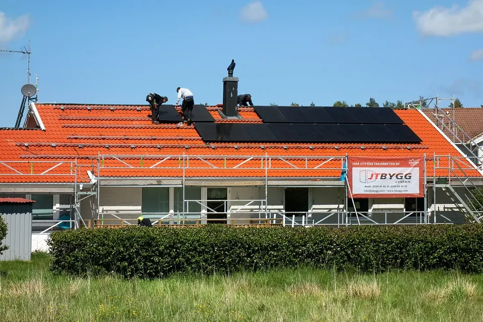 Maison au toit de tuiles orange en travaux, avec échafaudage et panneaux solaires installés sur une partie du toit