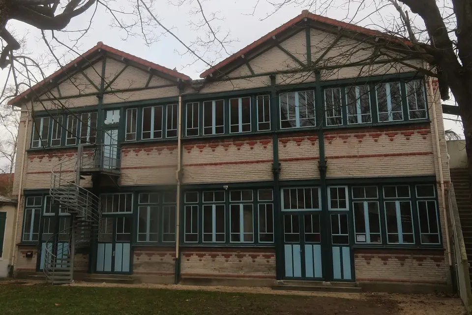 Bâtiment ancien en brique et pans de bois à deux pignons, grandes fenêtres vitrées et escalier extérieur métallique