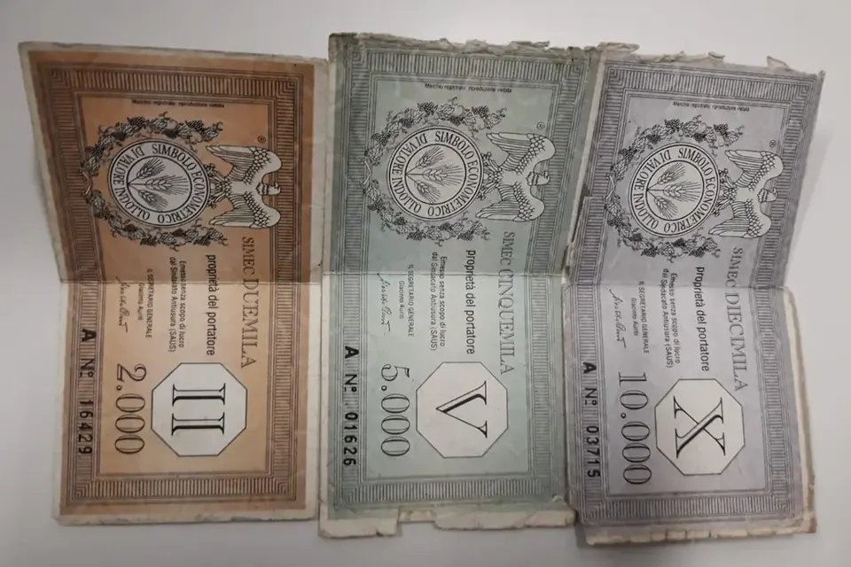 Trois billets anciens de couleur beige, verte et violette, de valeurs différentes, posés sur une table